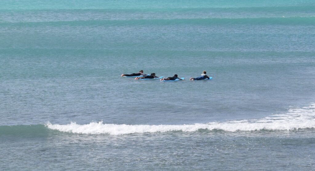 Surf instructor paddling out with three beginner surfers during a surf lesson in Boa Vista, Cape Verde
